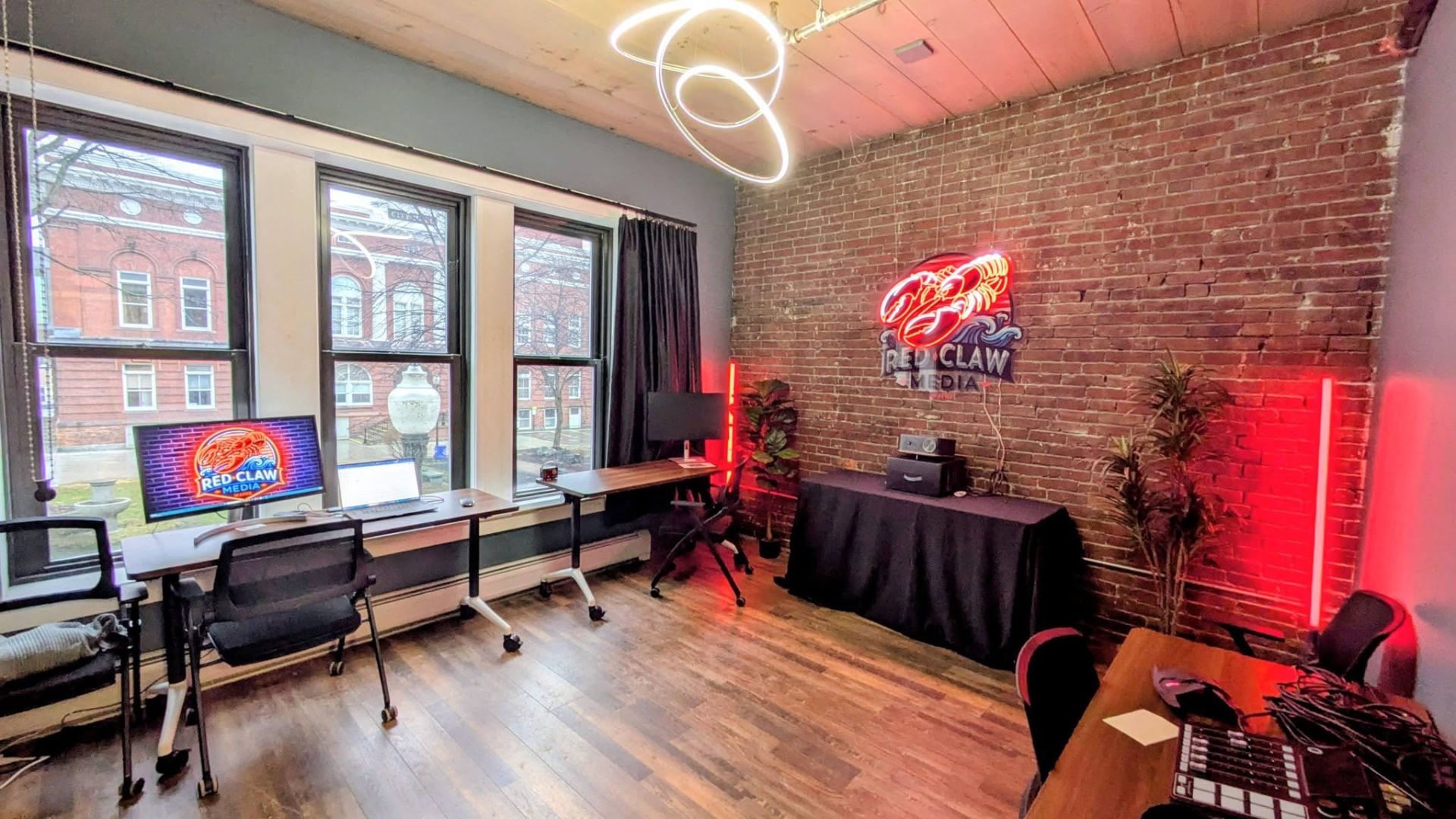 Red Claw Media edit suite in Waterville, Maine with neon lobster sign, exposed brick wall, red accent lights and editing desks